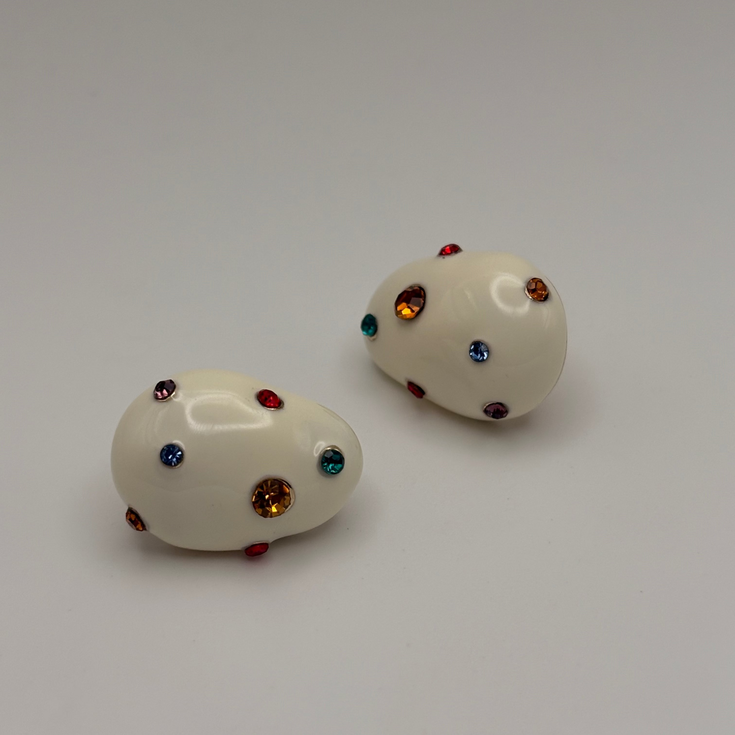 Pair of white earrings with multicolored gemstones on a light background