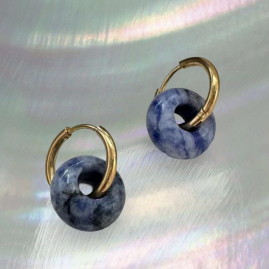 Pair of earrings with gold loops and blue spherical stones on a textured surface.