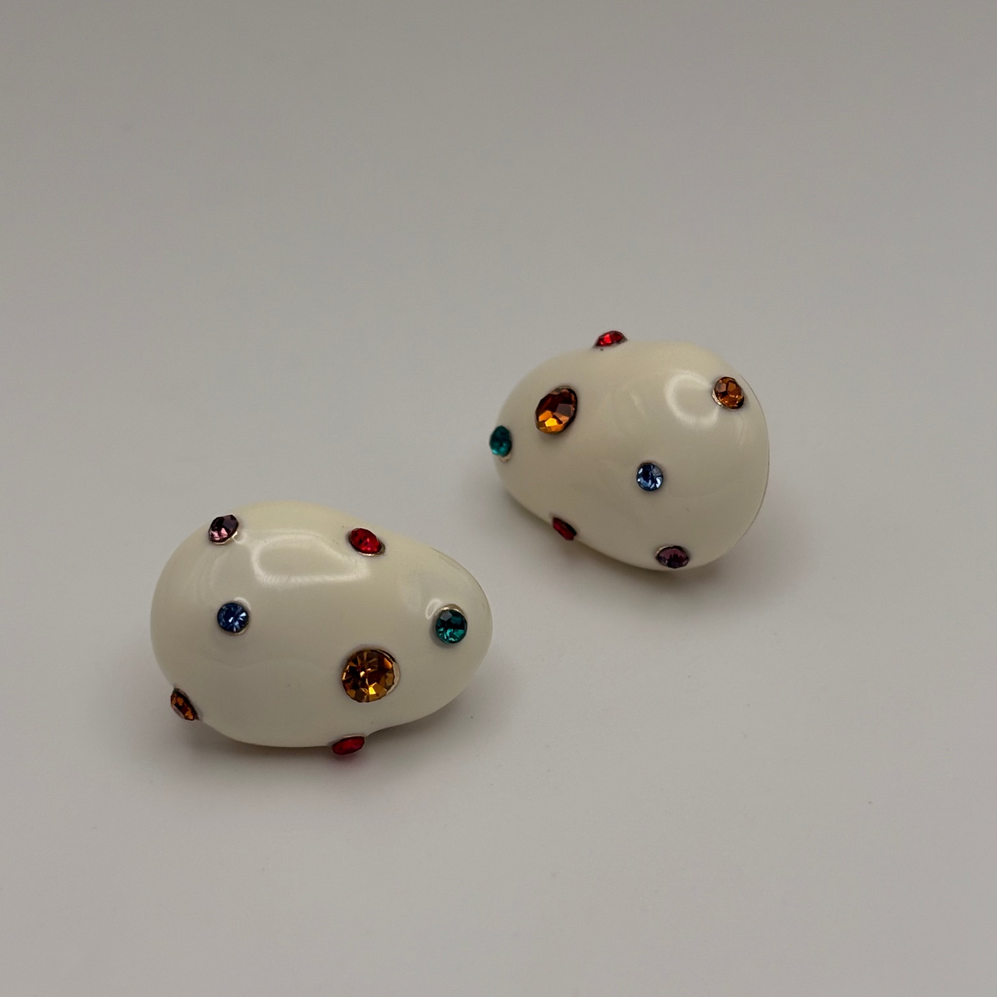 Pair of white earrings with multicolored gemstones on a light background