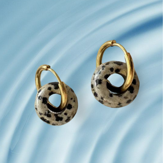 Pair of gold hoop earrings with black and white speckled stones on a blue water-like background