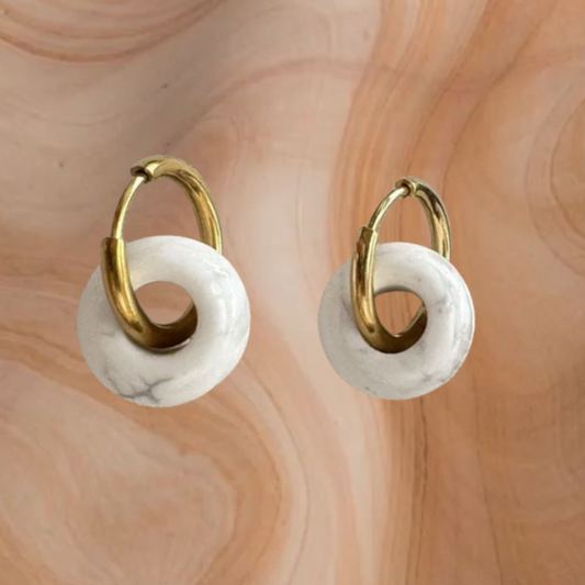 Gold hoop earrings with white circular stones on a marbled surface
