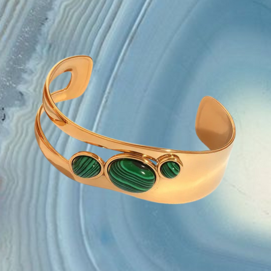 Gold cuff bracelet with green stones on a textured blue background
